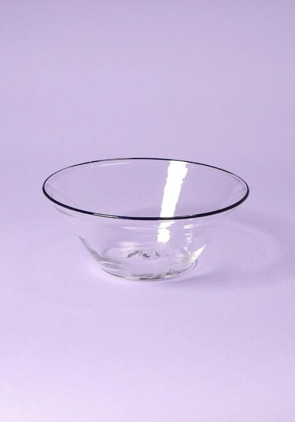 A clear glass bowl on a light purple background.
