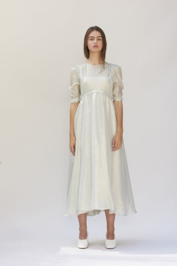 A woman wearing a shimmery long dress with puffed sleeves and white shoes.