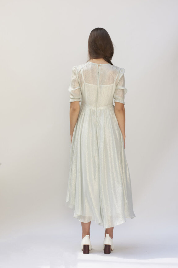A woman in a light, shimmery dress with long sleeves stands with her back to the camera.
