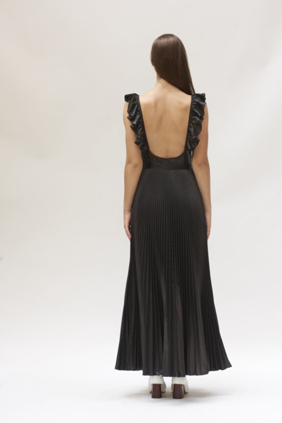 A person wearing a backless black pleated dress with ruffled straps, viewed from behind.