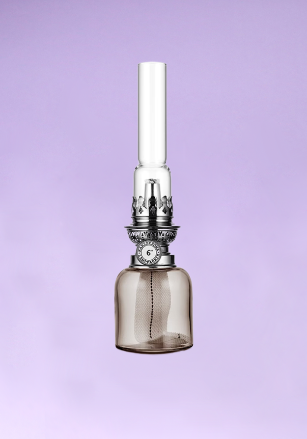 A vintage-style glass and metal oil lamp with a silver finish and patterned detailing, set against a light purple background.