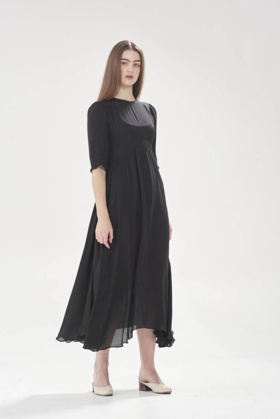 A woman wearing a long black dress with mid-length sleeves and beige heels.