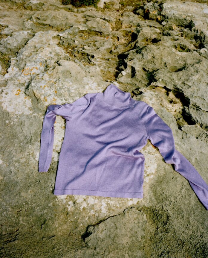 A lavender sweater is laid out on rocky ground.