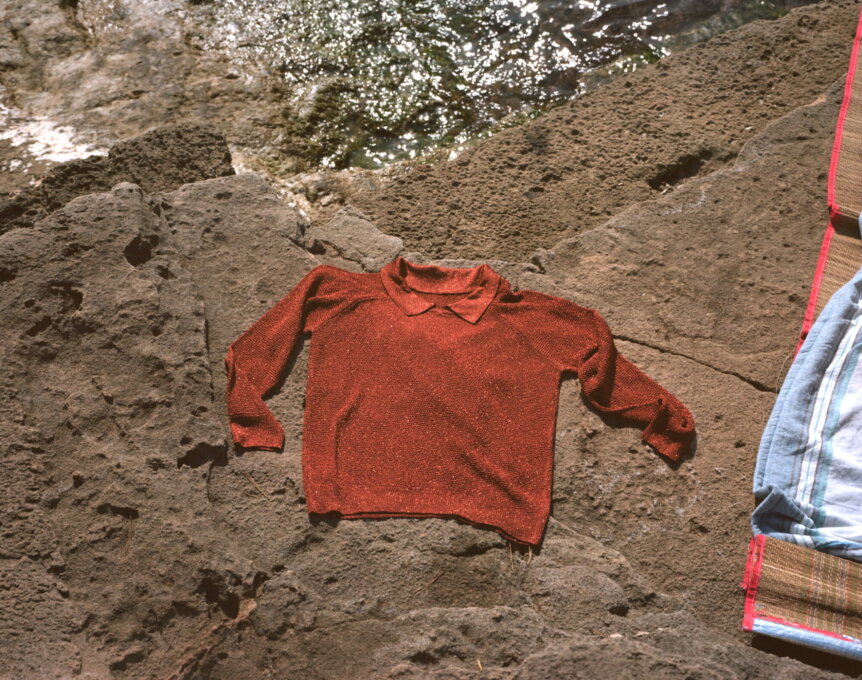 A red sweater is laid out on a rocky surface near the water.