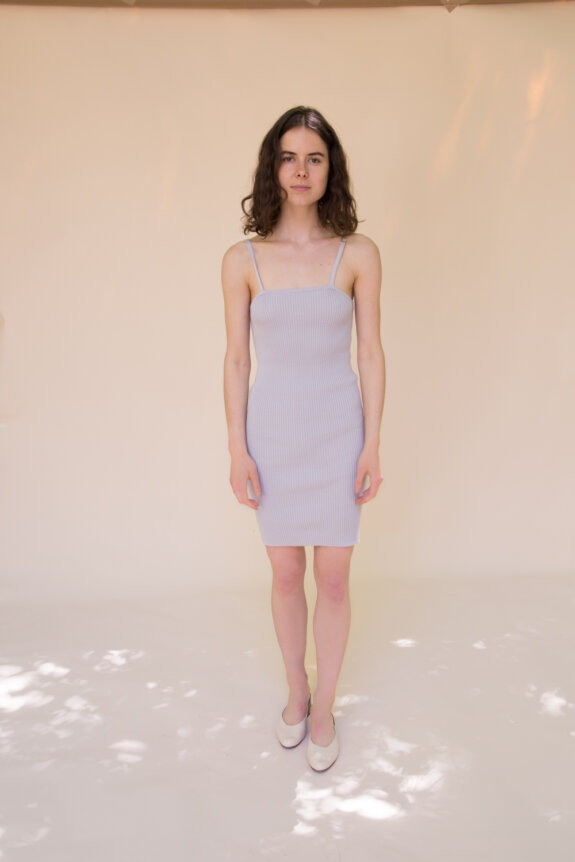 A woman in a light purple spaghetti strap dress stands against a plain background.