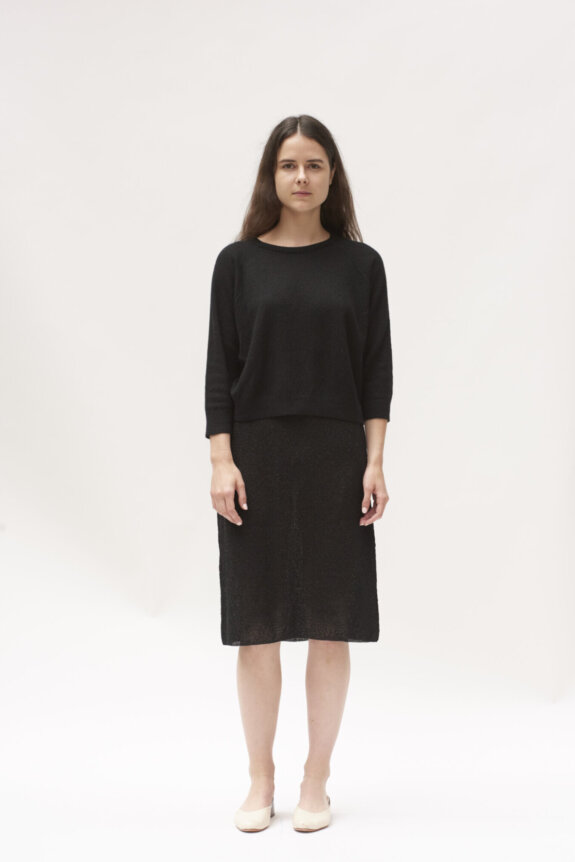 A woman in a black outfit standing against a plain white background.