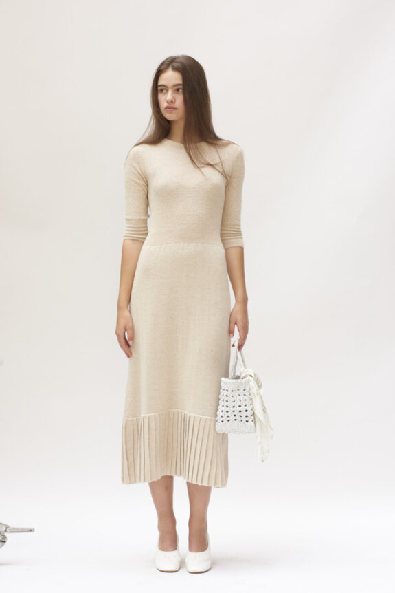A woman in a beige dress holding a crochet bag.