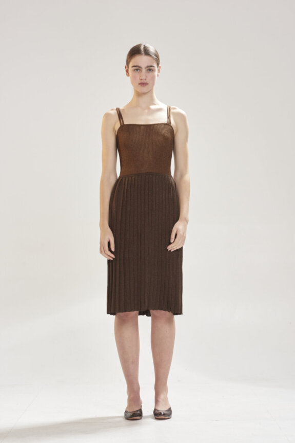 A model wearing a brown, ribbed, sleeveless dress with thin straps and black heels stands in a neutral setting.