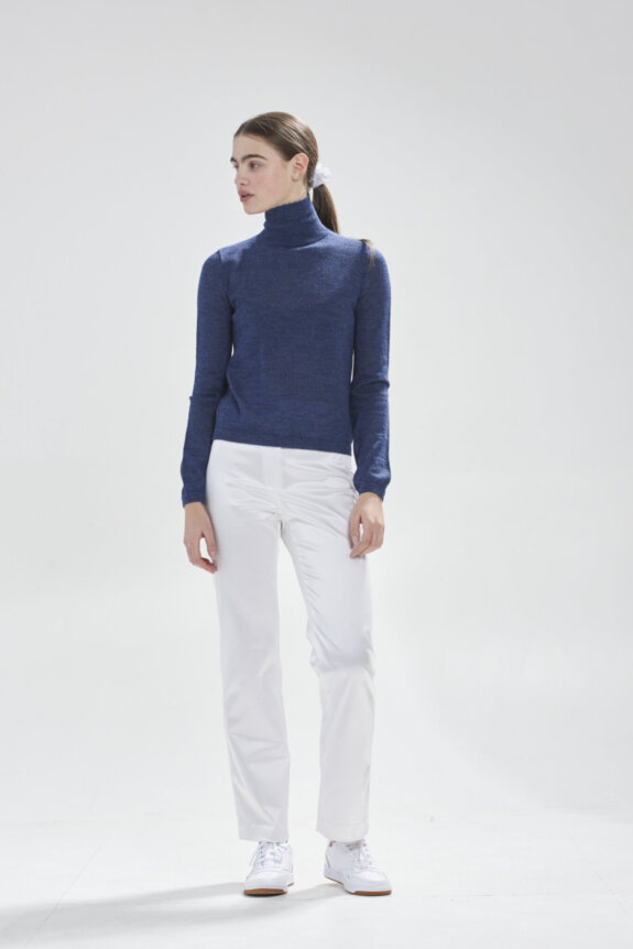A person wearing a blue turtleneck and white pants.