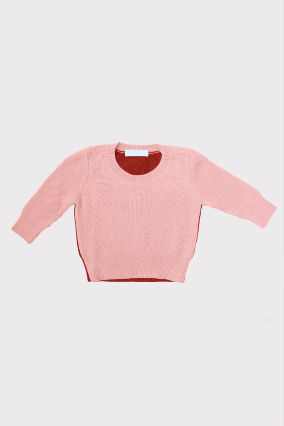 A pink knitted sweater with a red interior laid flat against a plain background.