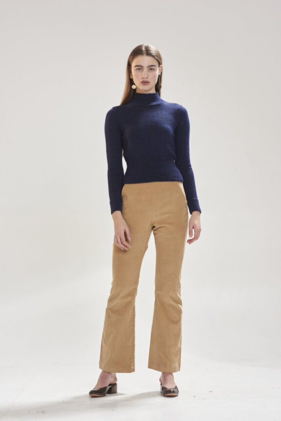A woman in a navy sweater and tan pants poses against a plain background.