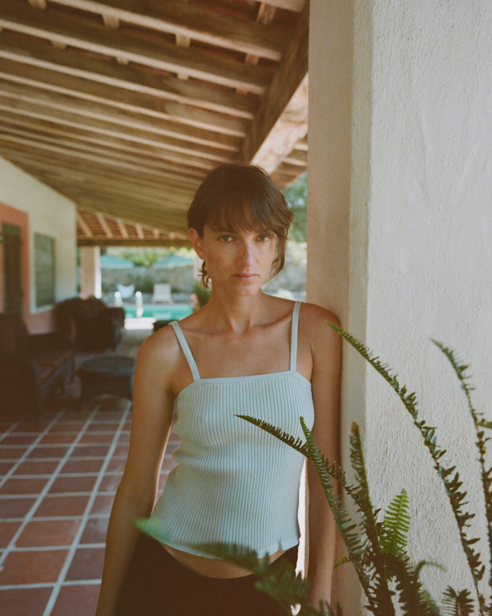 A person in a light blue top stands by a pillar on a covered patio.