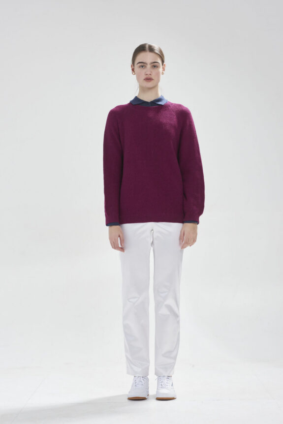 Person wearing a purple sweater, white pants, and sneakers against a plain background.