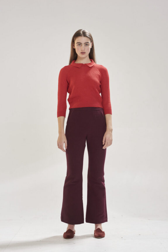 A person wearing a red sweater and dark red pants stands against a plain background.