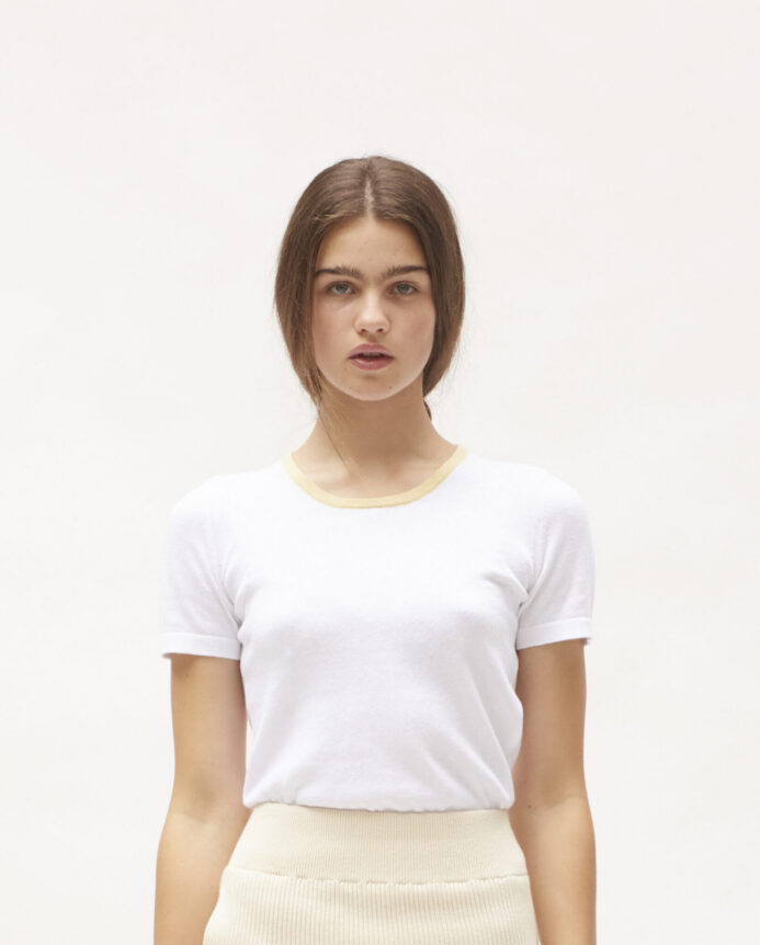 A person wearing a white T-shirt with beige trim, standing against a plain background.
